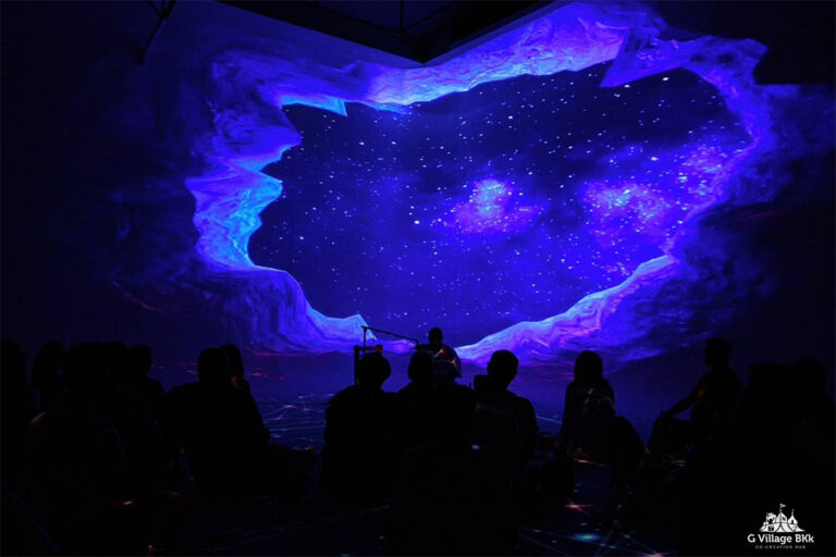นักดนตรีเล่นสดหน้าภาพถ้ำและท้องฟ้าดาวที่ฉายเต็มผนังใน Immersive Stage