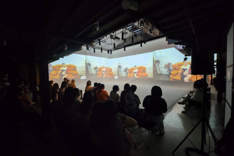 ผู้ชมนั่งดูการแสดงหน้าภาพฉายเต็มผนังใน The Circus Studio