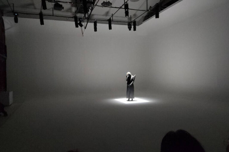 นักแสดงเดี่ยวยืนใต้สปอตไลต์กลางห้องขาวที่ The Circus Studio