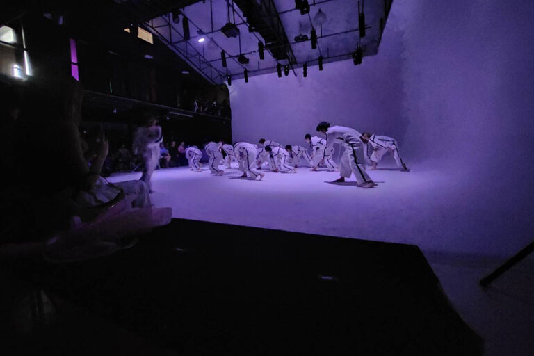 นักเต้นในชุดขาวแสดงใต้ไฟสีม่วงที่ The Circus Studio