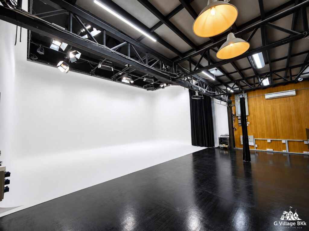 มุมกว้างของ The Stage Studio เห็นฉากขาว พื้นที่ทำงานและโครงไฟ