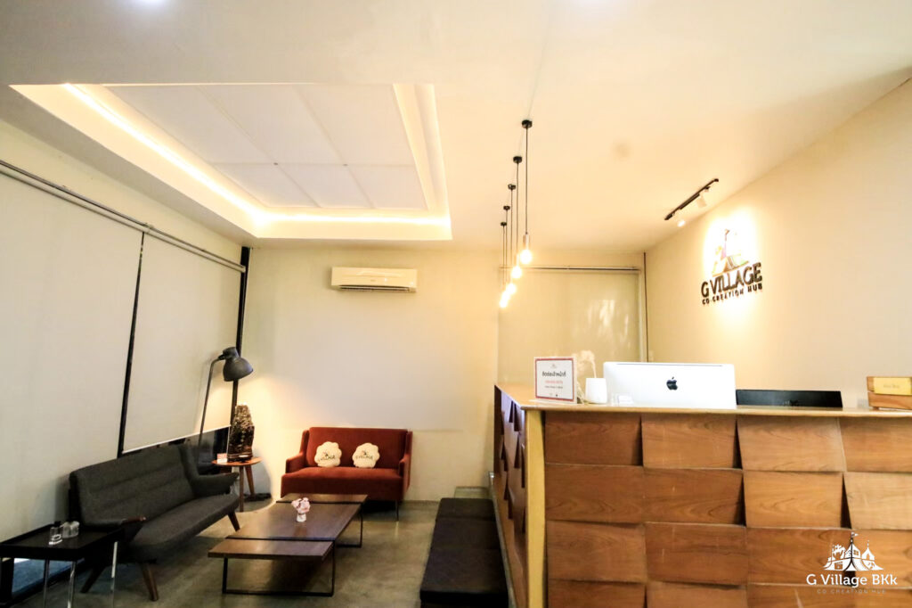 RECEPTION เคาน์เตอร์ต้อนรับไม้ ป้าย G Village และมุมนั่งรอ